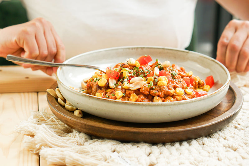 Eine Schale Erdnuss-Quinoa-Gericht mit Mais, Paprika und gerösteten Erdnüssen